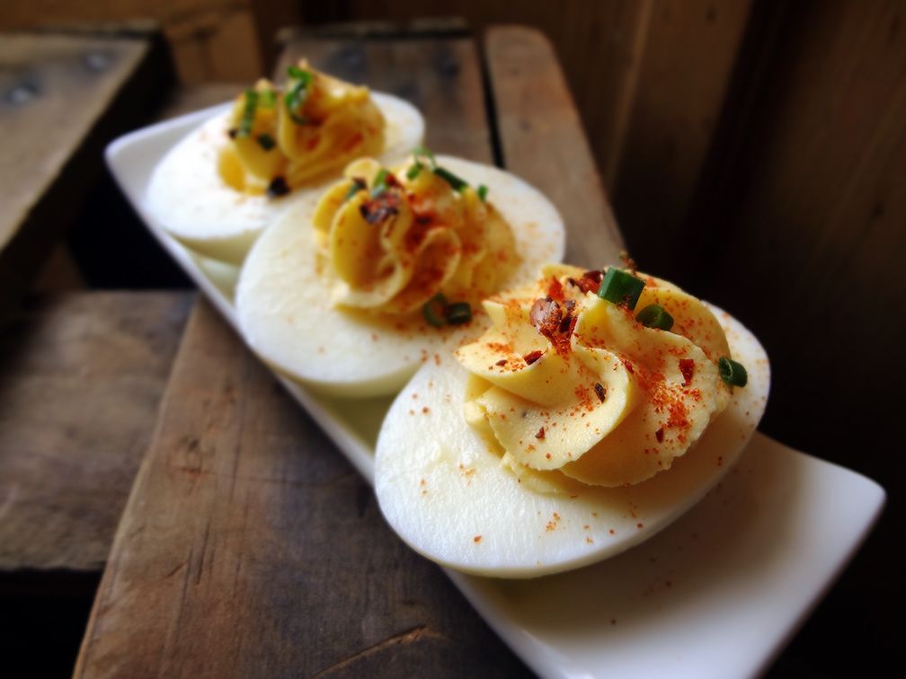 Three deviled eggs topped with paprika and chives on a white rectangular platter atop a rustic wooden surface.