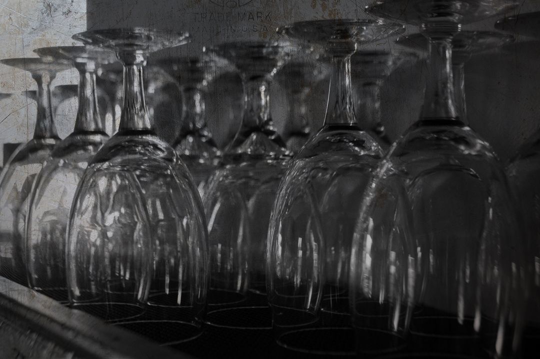 A row of clear wine glasses turned upside down and lined up on a shelf.