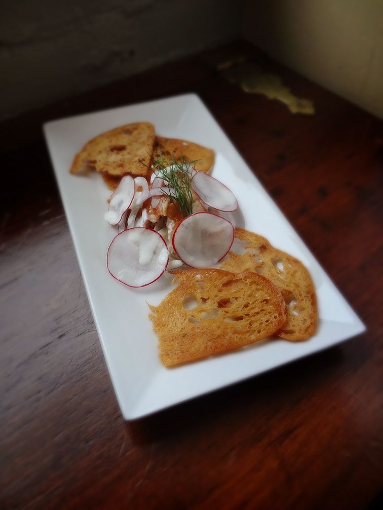 A rectangular white plate holds a fish tartare appetizer garnished with thin radish slices and served with toasted bread.