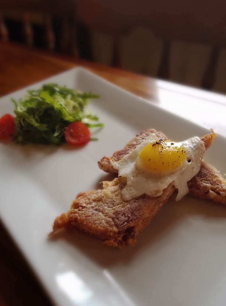 A small fried egg on two strips of toasted bread with a side of green salad and cherry tomatoes on a white rectangular plate.
