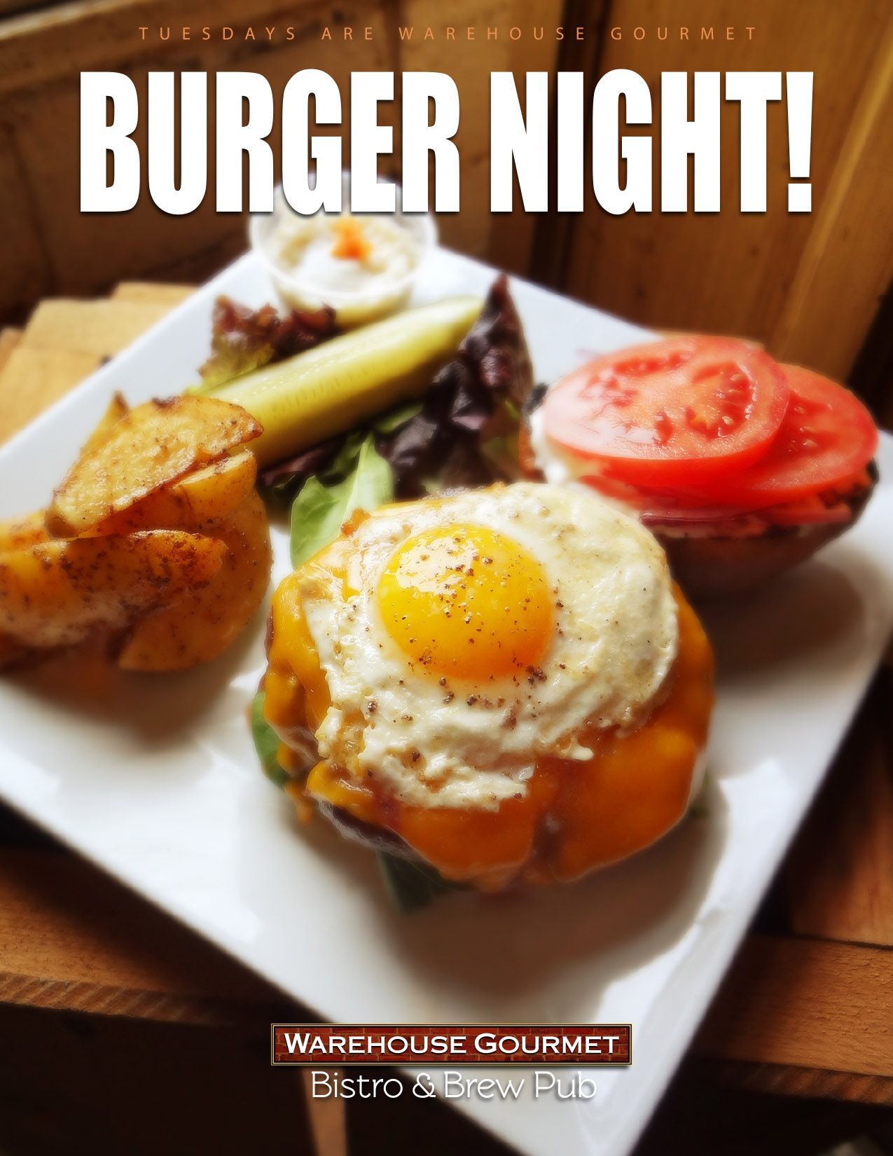 A burger topped with a fried egg and cheese, served with wedges, a pickle, and tomato at Warehouse Gourmet Bistro.