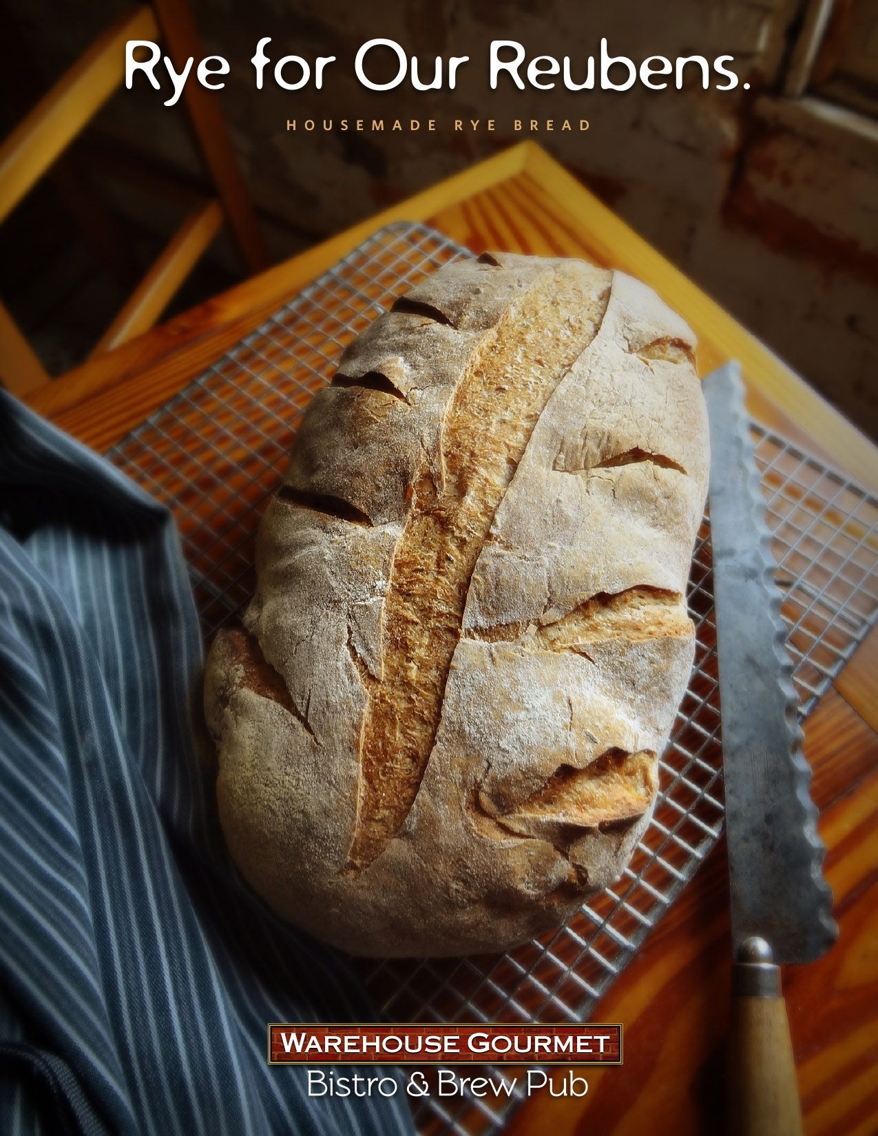 A loaf of rye bread sits on a cooling rack next to a bread knife and a cloth, with the Warehouse Gourmet logo above.