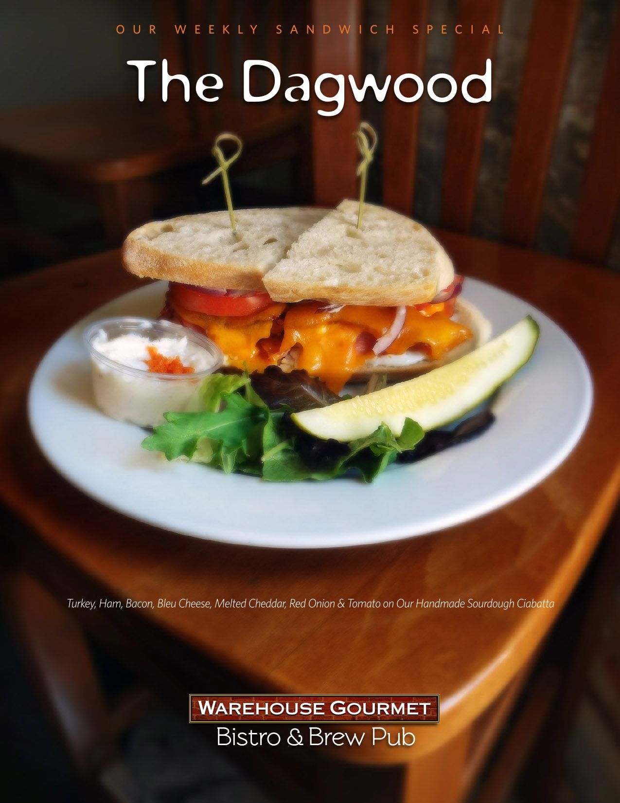 A Dagwood sandwich, side of sauce, and pickle slice on a plate at Warehouse Gourmet Bistro & Brew Pub.
