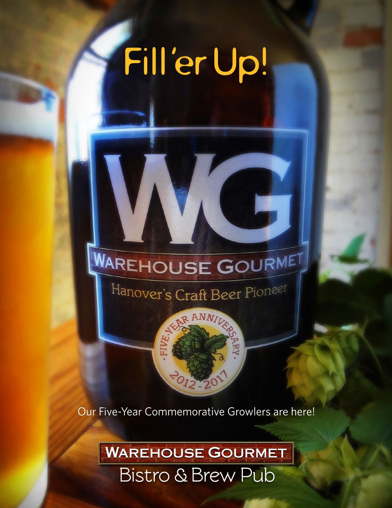 A Warehouse Gourmet commemorative growler with a 5th-anniversary logo next to a beer glass and fresh hops.