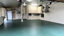 Spacious garage with green epoxy floor, white walls, storage cabinets, and a mounted bicycle.
