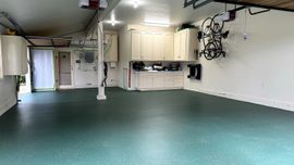 Spacious garage with green epoxy floor, white walls, storage cabinets, and a mounted bicycle.