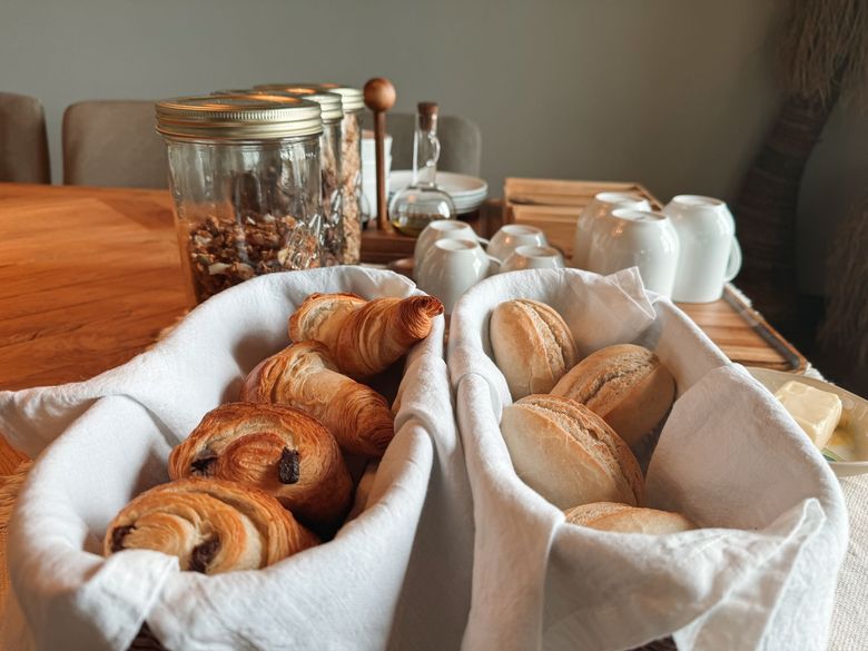 Breakfast spread: Baskets of pastries, croissants, rolls, nuts, milk, and butter on a wooden table.