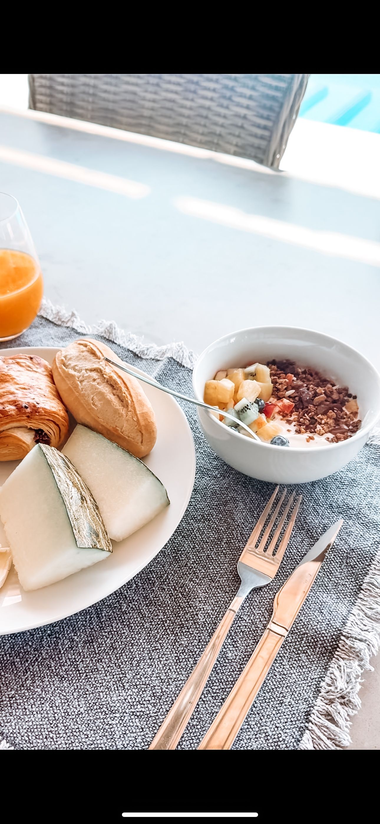 Breakfast spread with cheese, bread, yogurt bowl, and orange juice on a placemat, with cutlery on the side.