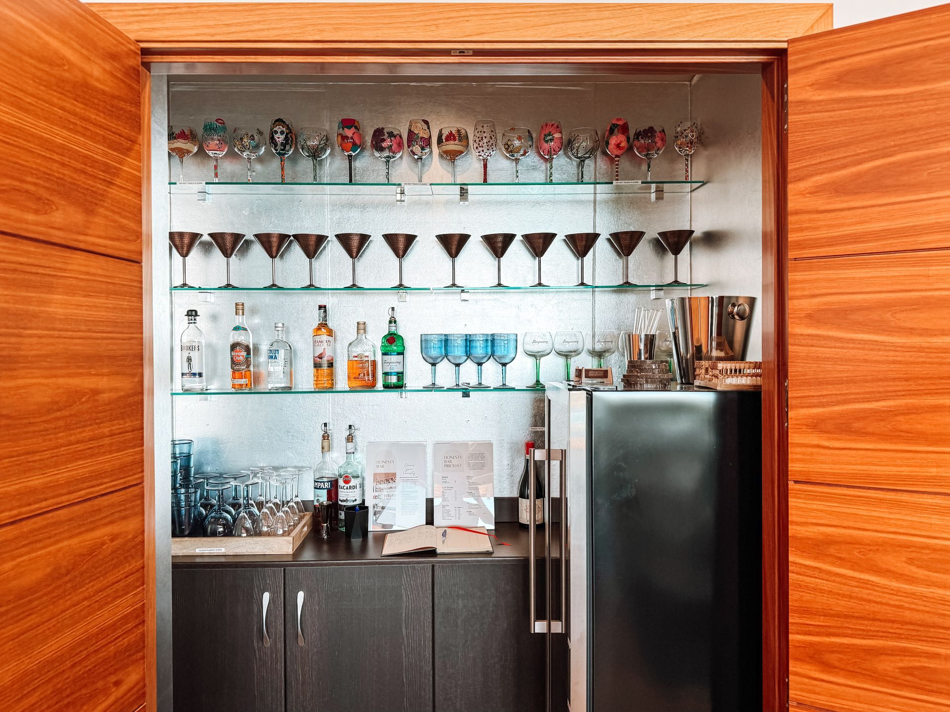 Built-in home bar with shelves of glasses, bottles, and cocktail accessories, framed by wood doors.