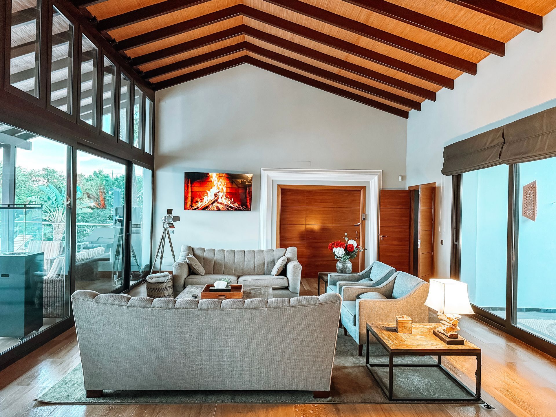 Living room with large windows and a vaulted ceiling. Two gray sofas face a coffee table, with a fireplace and TV on the wall.