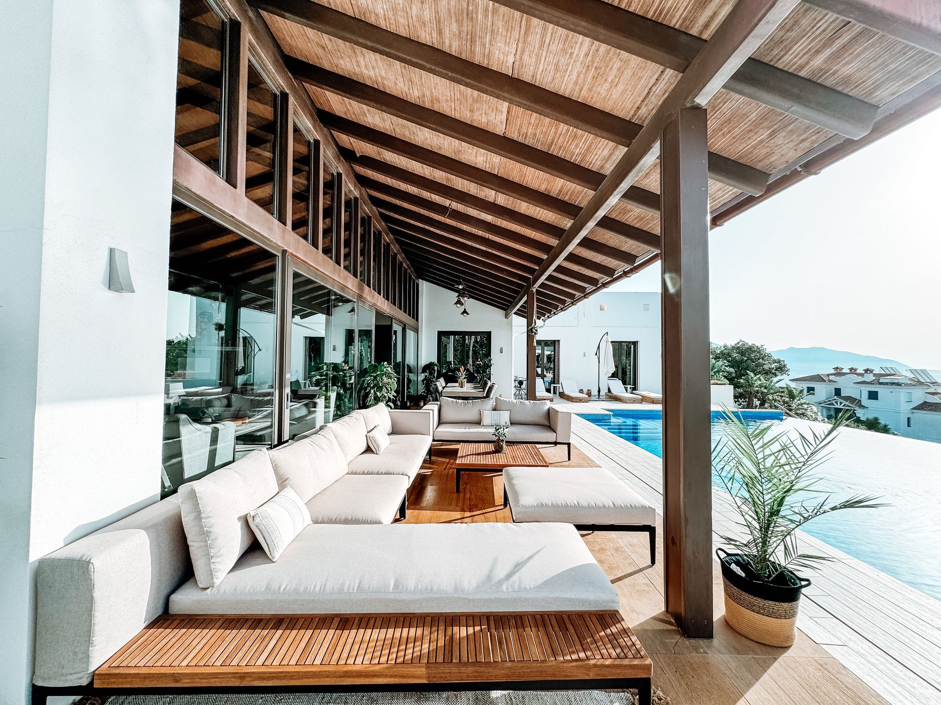 Outdoor seating area with a view of a pool and surrounding landscape.  A large sectional sofa sits under a covered patio.