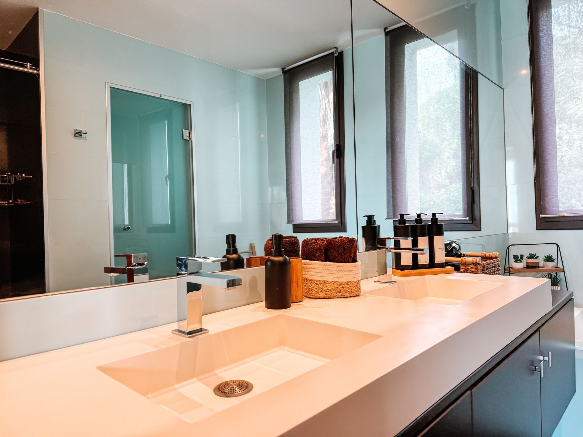 Modern bathroom with a large mirror over a double sink vanity and a glass-doored shower stall; walls are light blue.