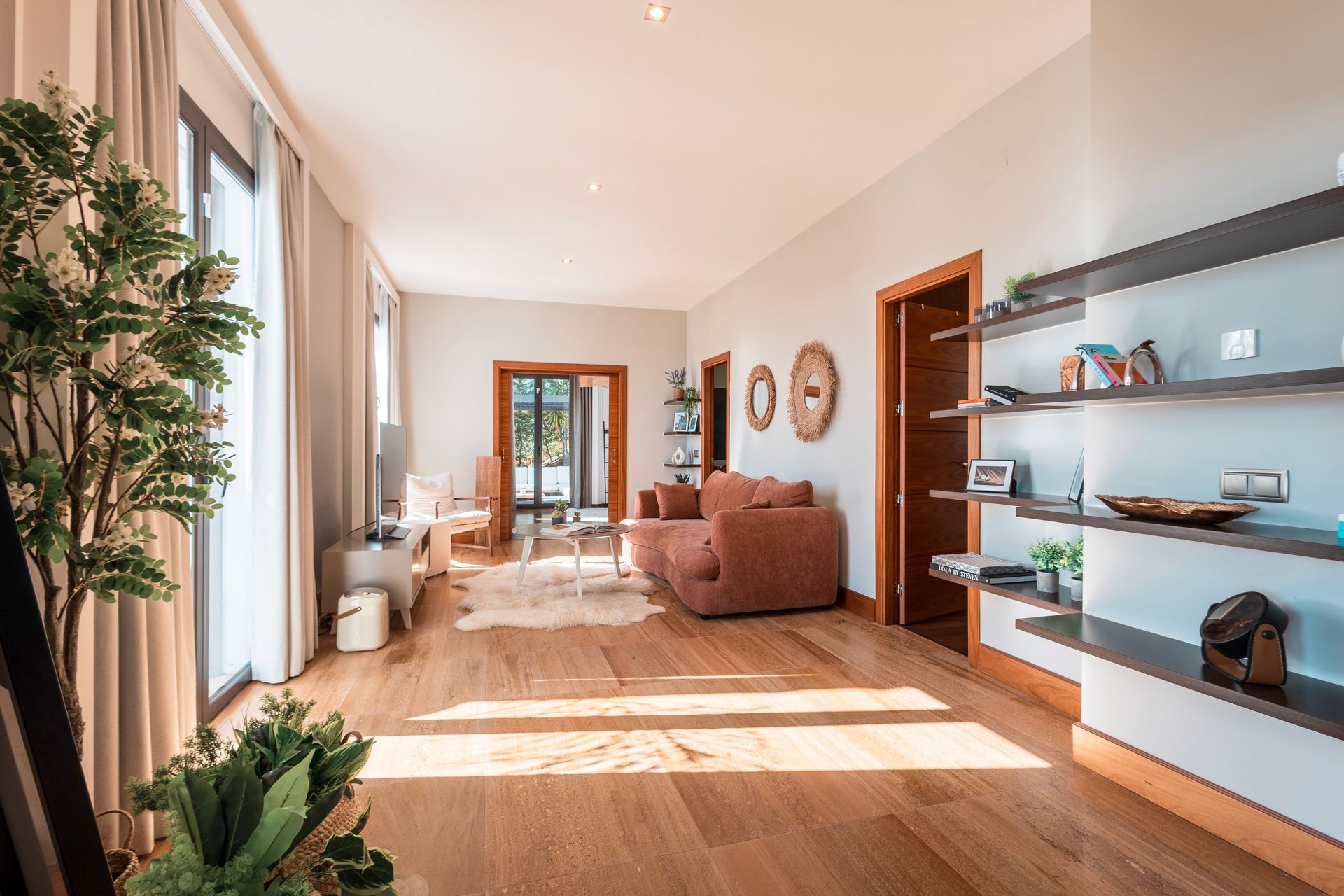 Spacious living room with hardwood floors, large windows, a pink sofa, and a decorative shelf filled with objects.