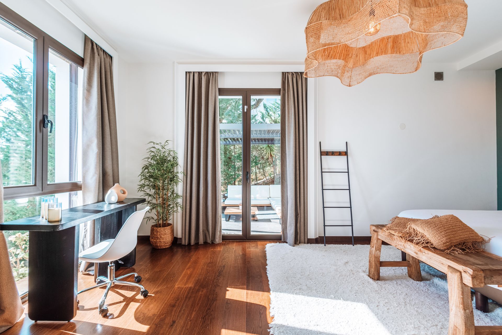 Bright, modern room with dark wood floors, a desk by a window, and a seating area on a rug. Neutral tones with a natural, textured light fixture.