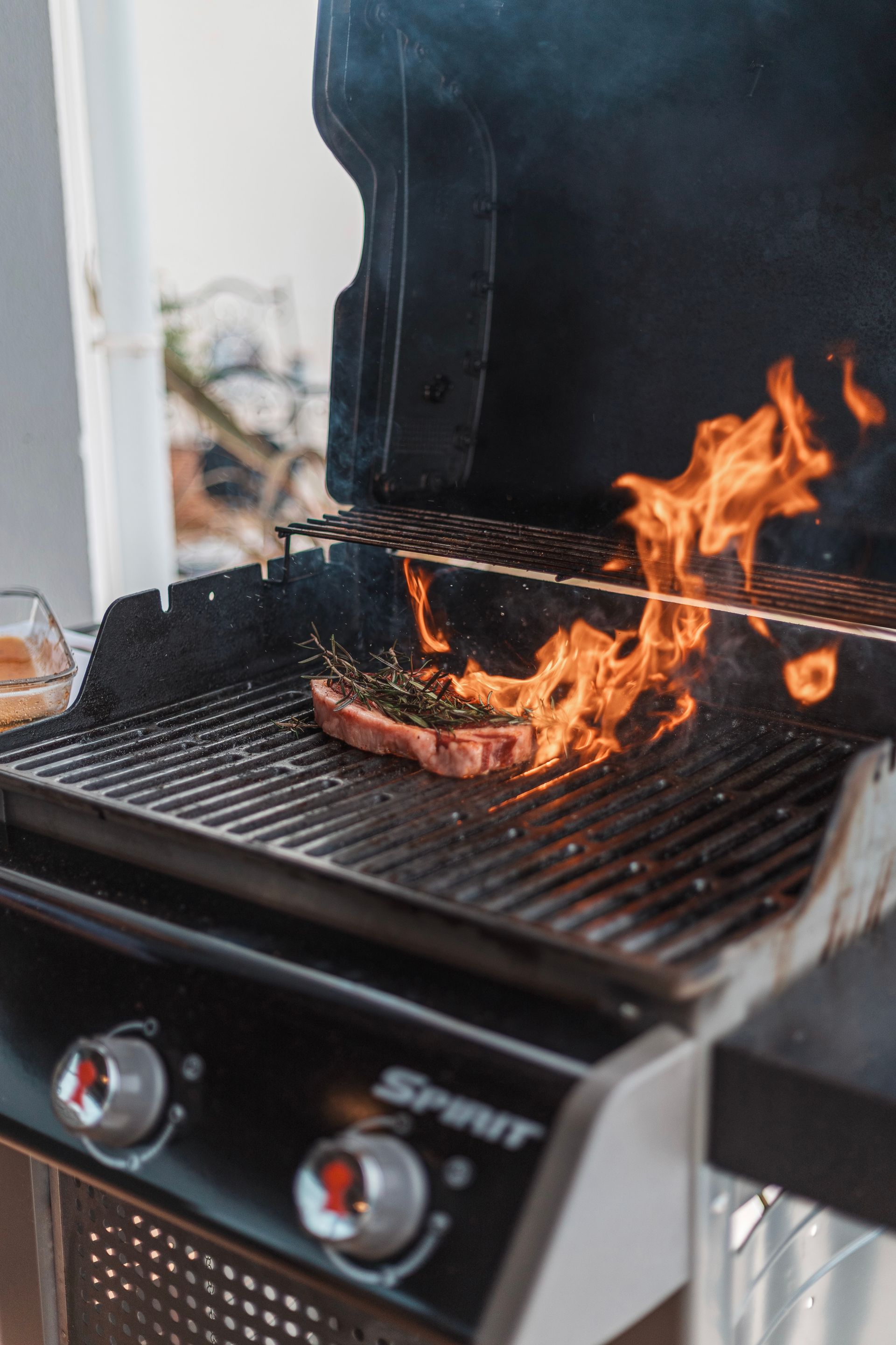 A steak on a grill with flames erupting; outdoor setting.