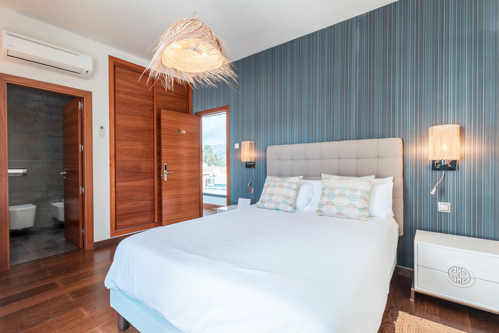 Bedroom with a blue striped wall, a bed with white linens, a light fixture, and wood doors and floors.