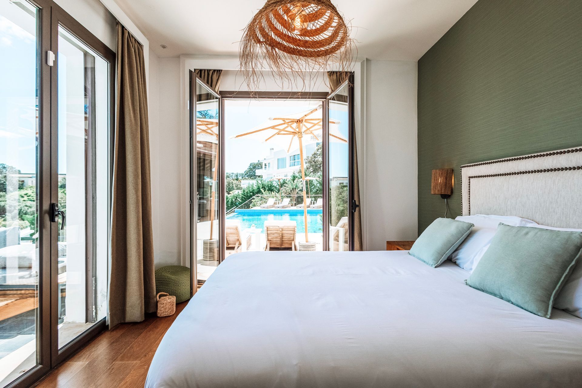 Bedroom with a large bed, open doors to a pool area, and a decorative light fixture.