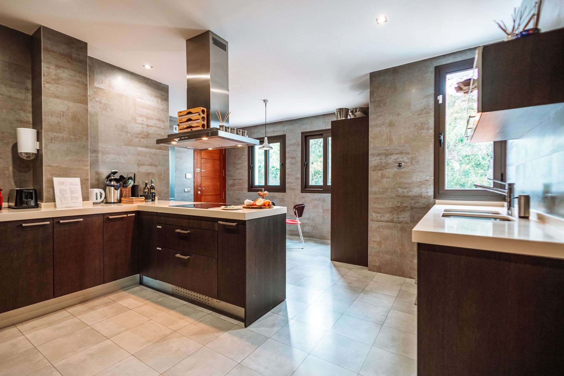 Modern kitchen with dark wood cabinets, light countertops, and gray tile walls and floors. Stainless steel range hood.