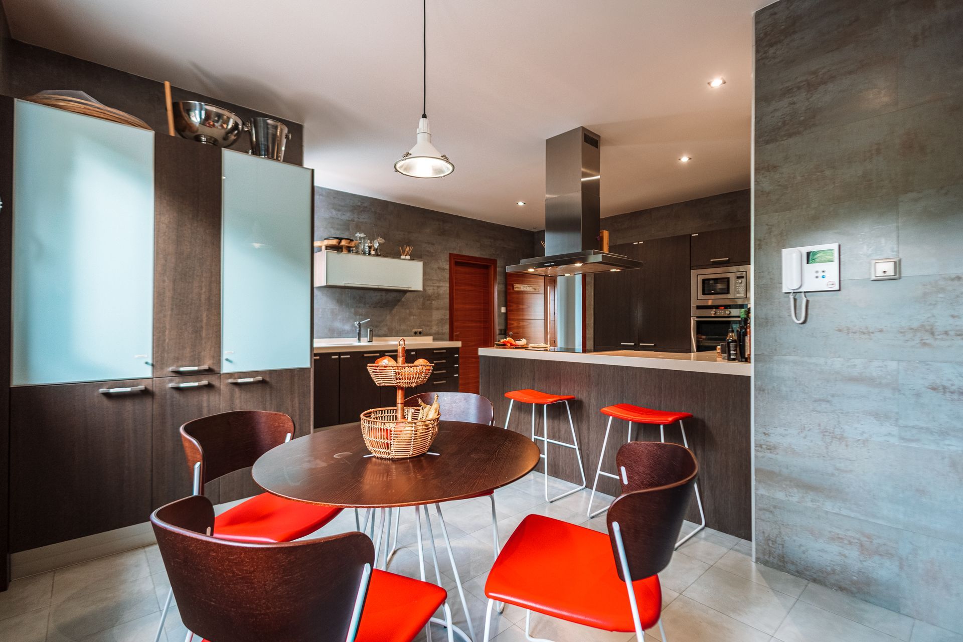 Modern kitchen with a round table and red chairs. Dark cabinets, gray walls, and a stainless steel range hood.