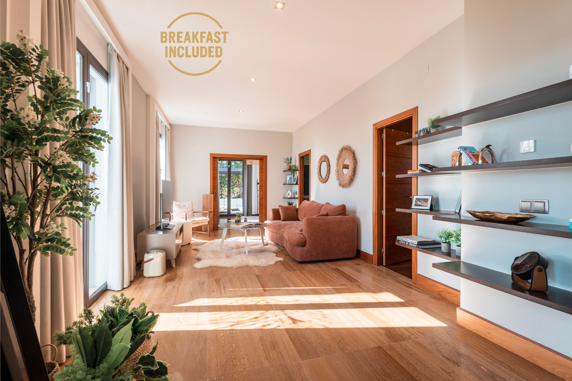 Bright living room with hardwood floors, large windows, and a coral sofa. Includes decorative shelves, plants, and access to a balcony.