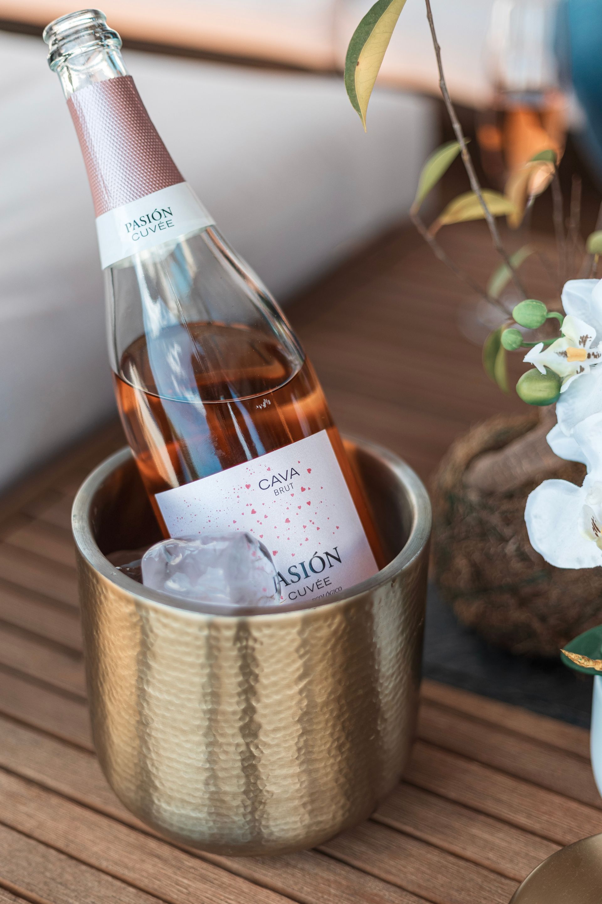 A bottle of rose sparkling wine chills in a gold bucket on a wooden surface.