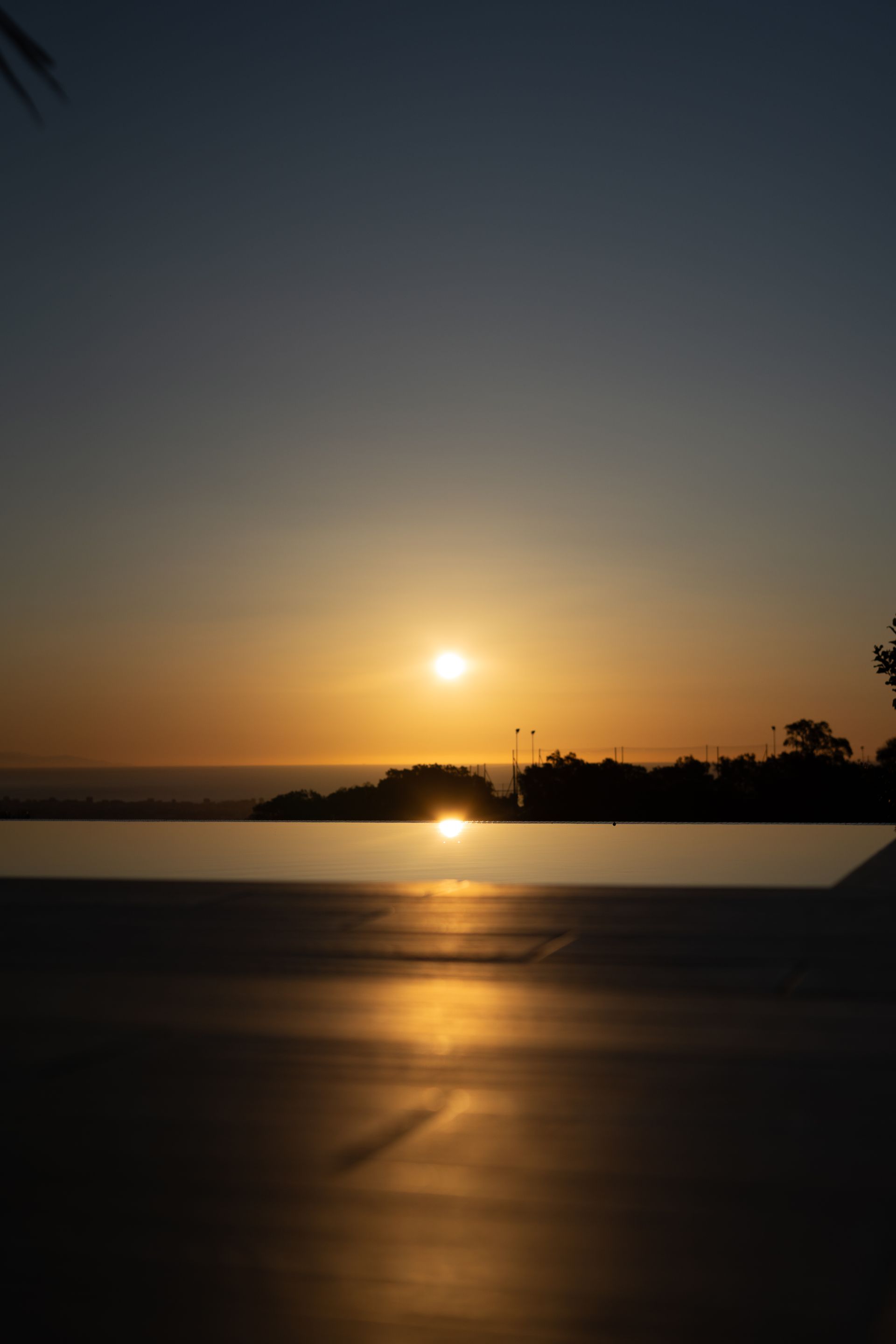 Sunset over a body of water, reflecting golden light. Silhouette of land against the bright sun in a clear sky.