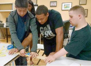 a group of young men are standing around a table working on a project .