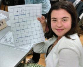 a young girl is holding a piece of paper with a grid on it .