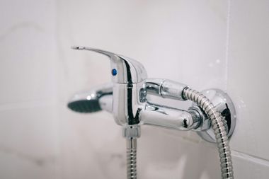 Close-up of a chrome wall-mounted shower faucet and mixing valve on white tiled walls.
