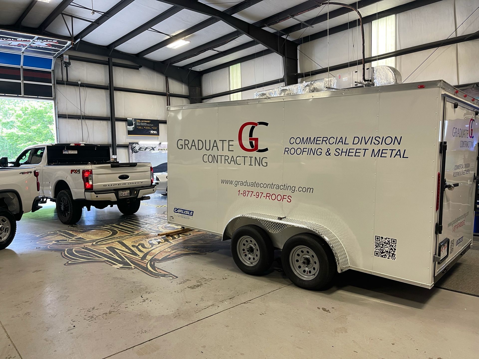 A white trailer is parked in a garage next to a truck.