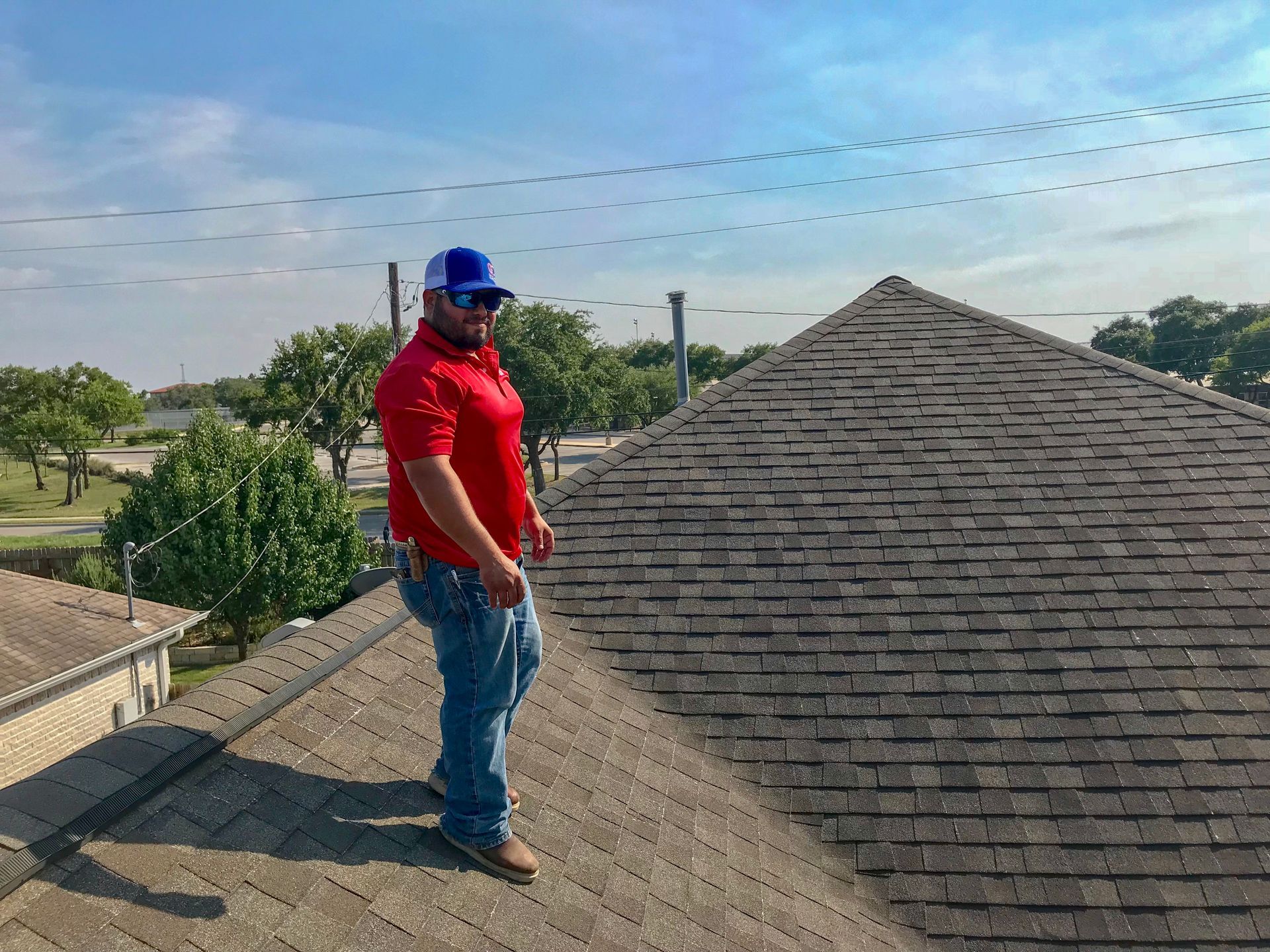 A man in a red shirt and blue hat is standing on top of a roof.