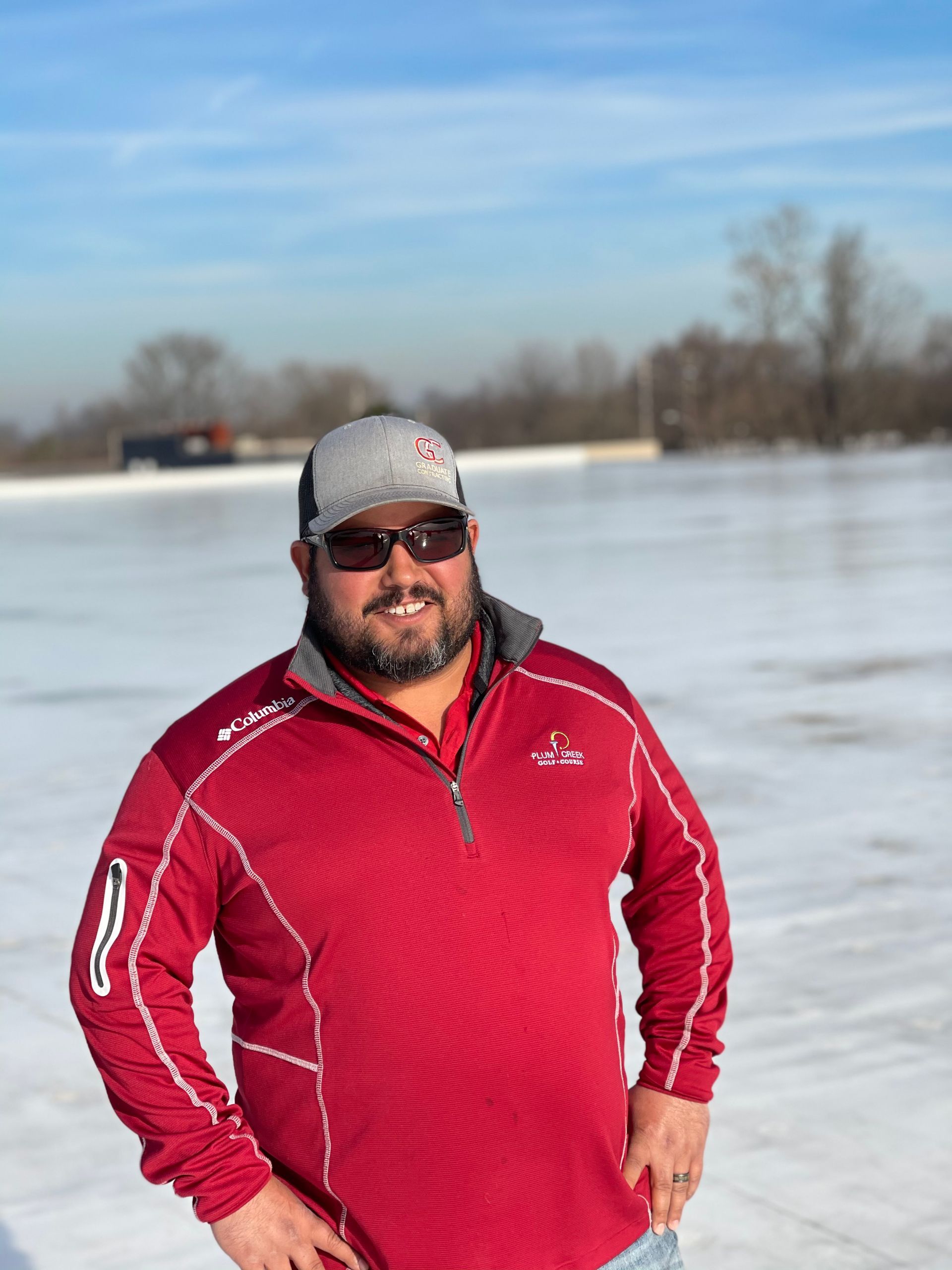 A man wearing sunglasses and a red jacket is standing on a commercial roof.