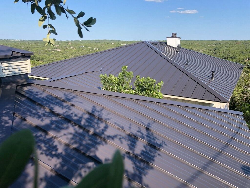 Dark metal roof with chimney, trees in background.