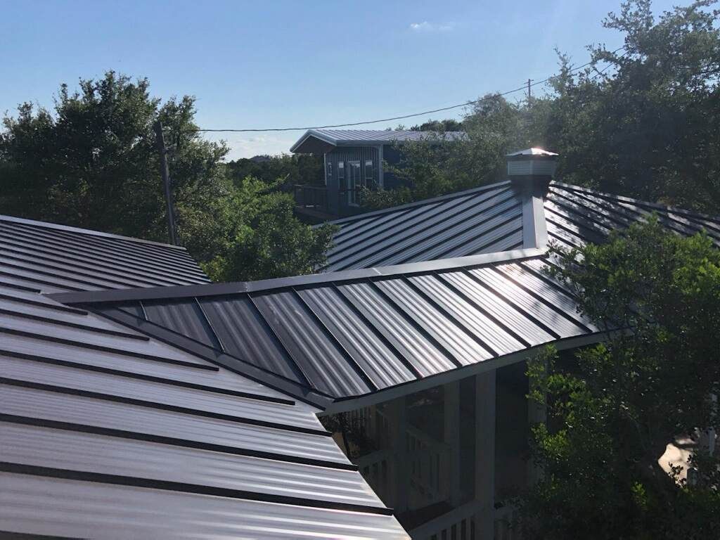 A house with a metal roof is surrounded by trees and a body of water.