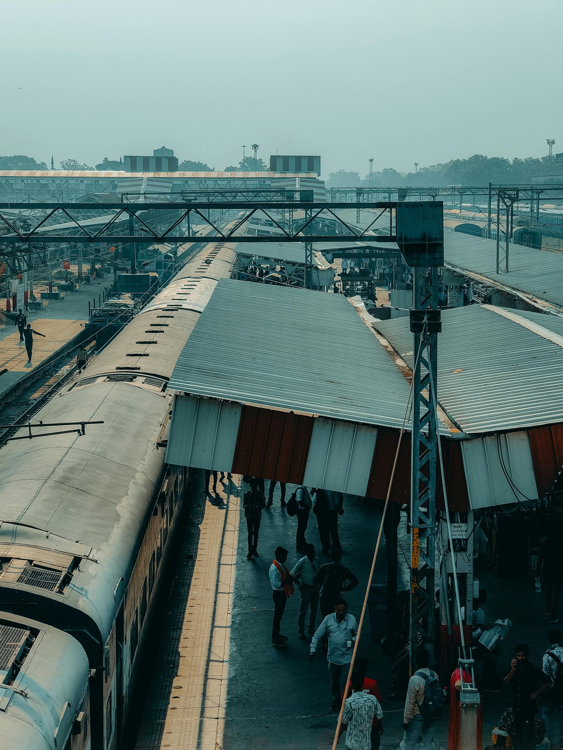 Train at a crowded train station with red and white striped roofs. People stand on the platform.