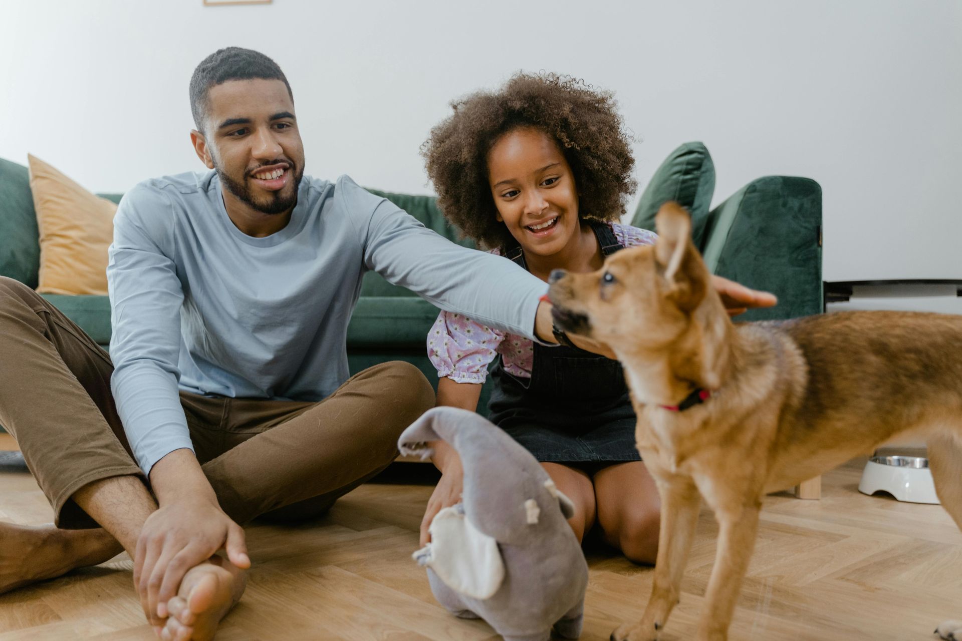 Two people sitting on the floor playing with a dog and stuffed toy in a living room