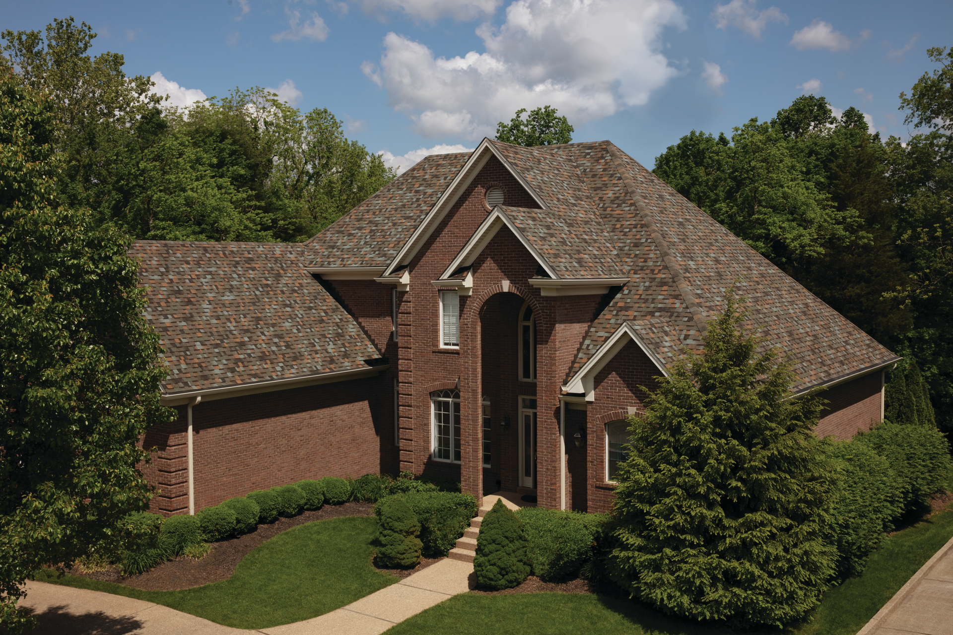 A large brick house with a brown roof is surrounded by trees.