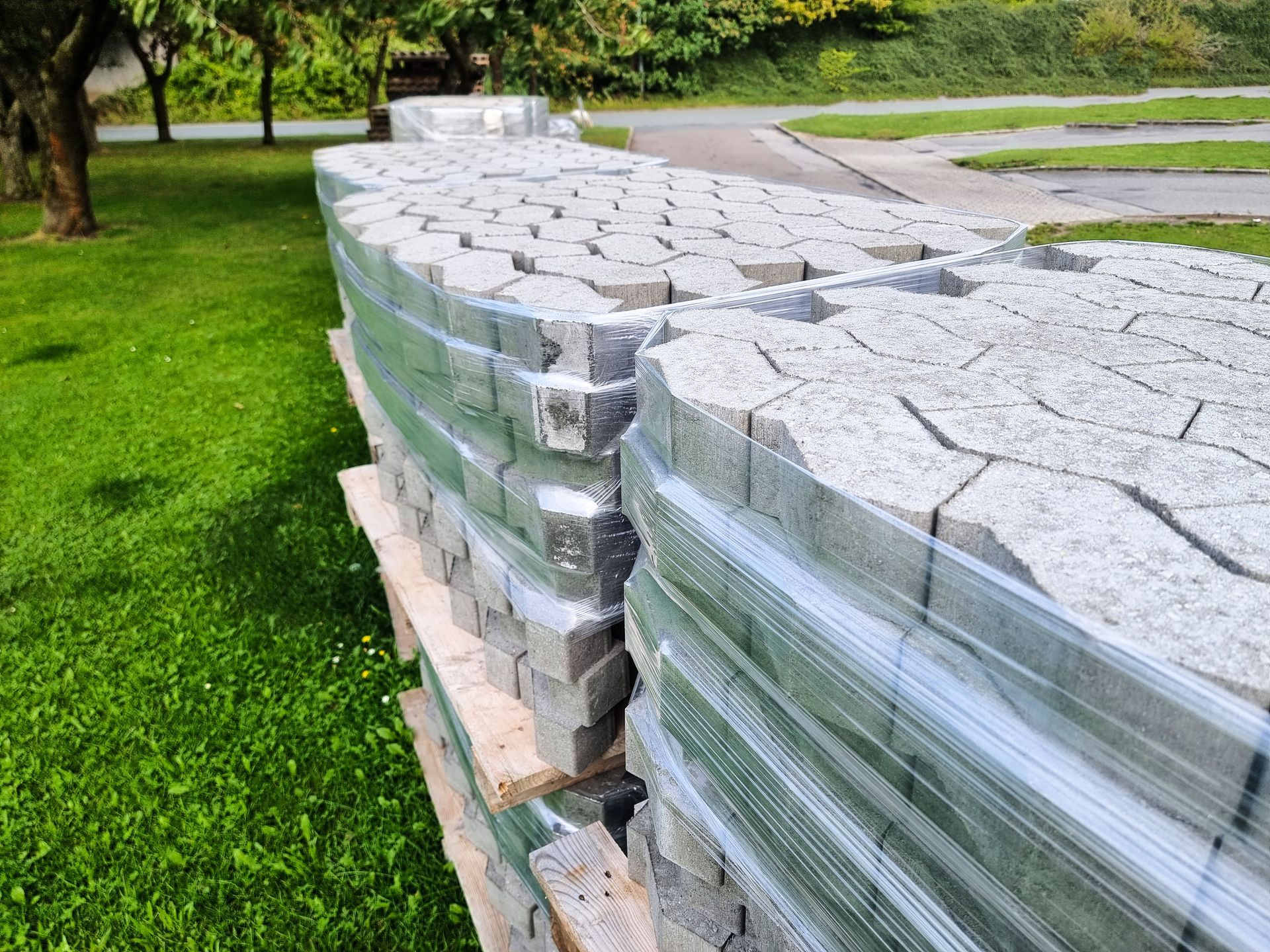 Pallets of gray paving stones wrapped in clear plastic on grass.