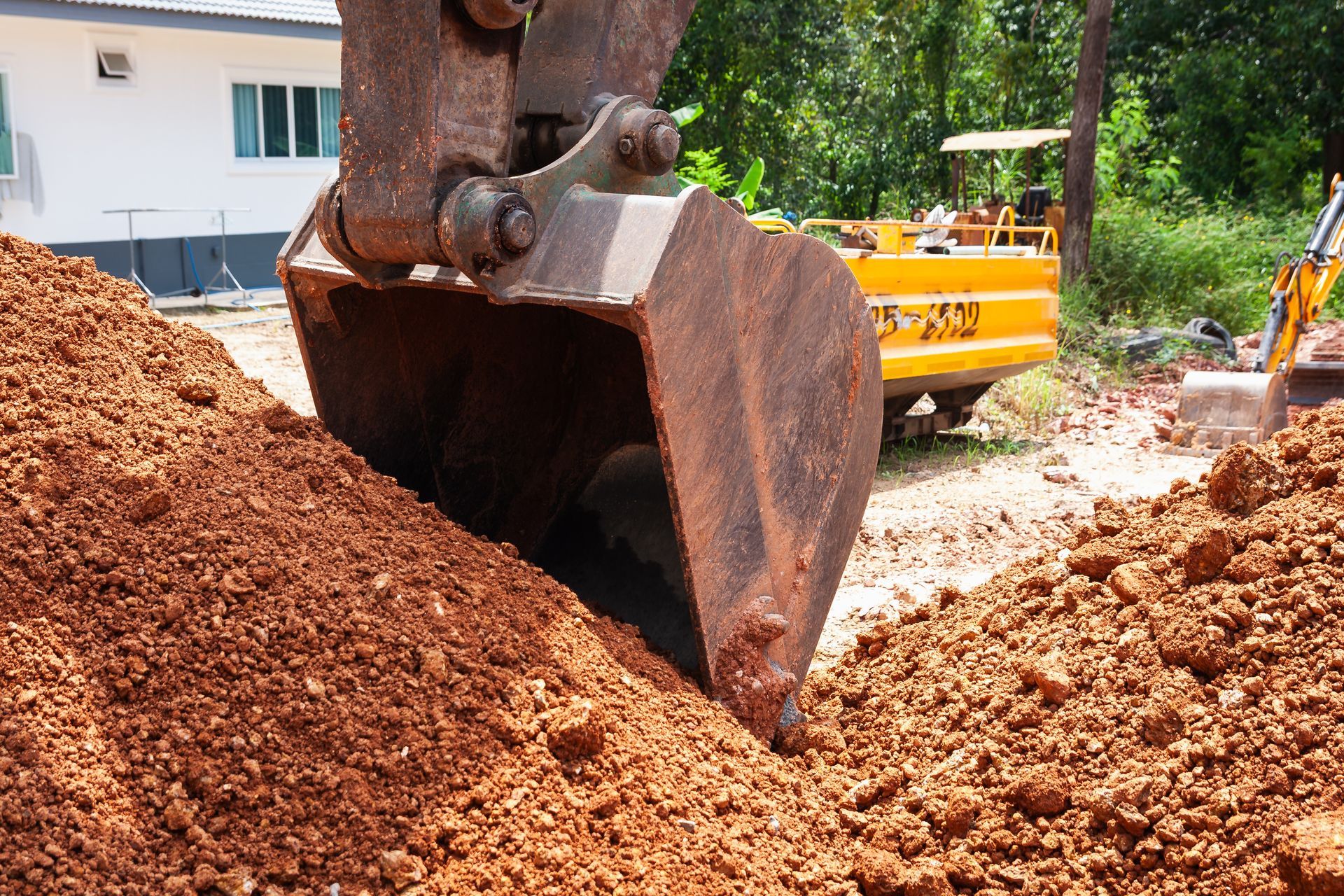 Excavator bucket digging into reddish-brown soil at a construction site