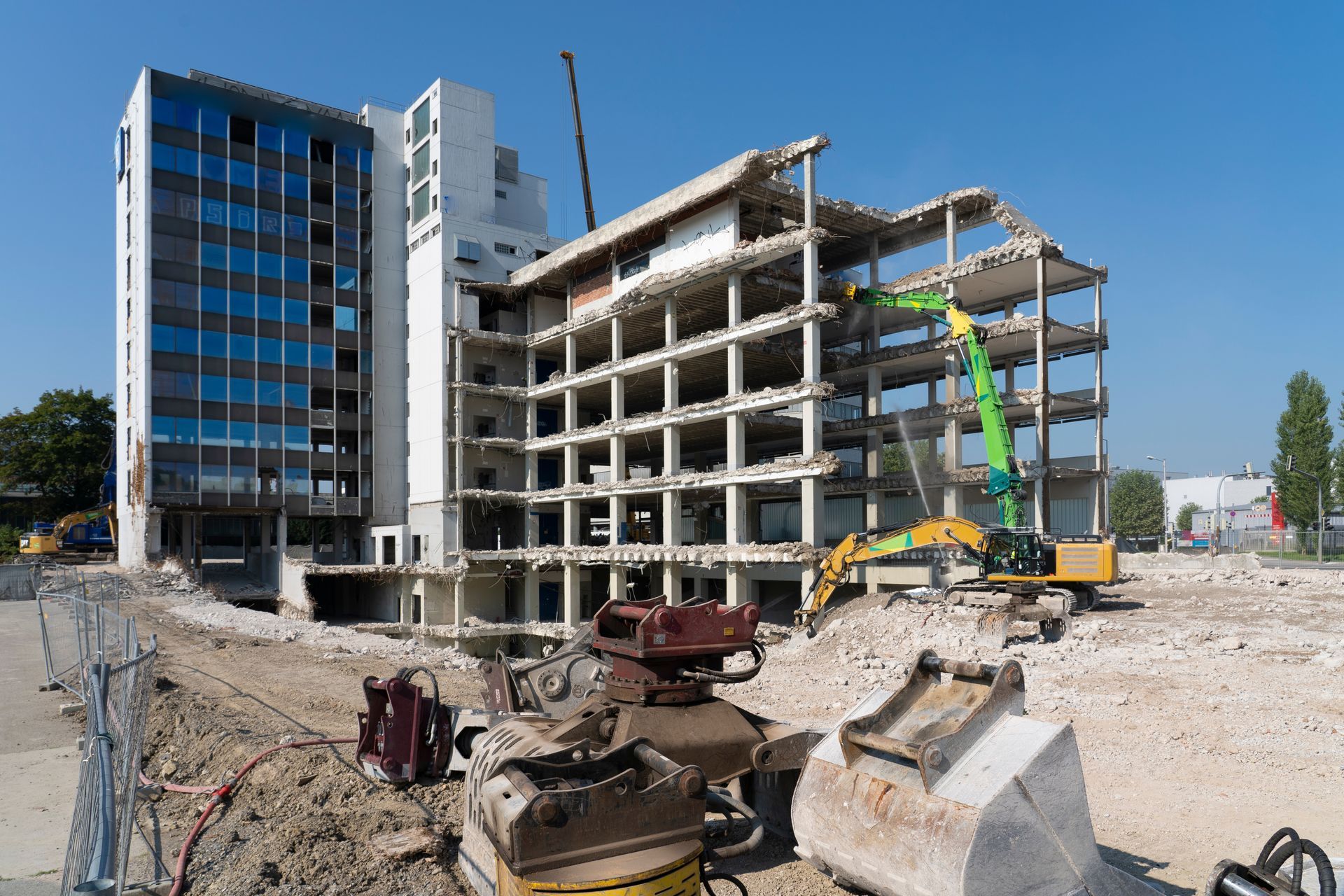 Building demolition in progress with heavy machinery; blue-windowed tower remains intact.