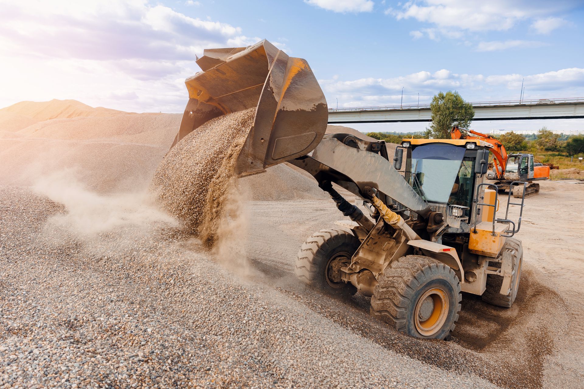 Yellow loader dumping gravel onto a large pile on a sunny day.