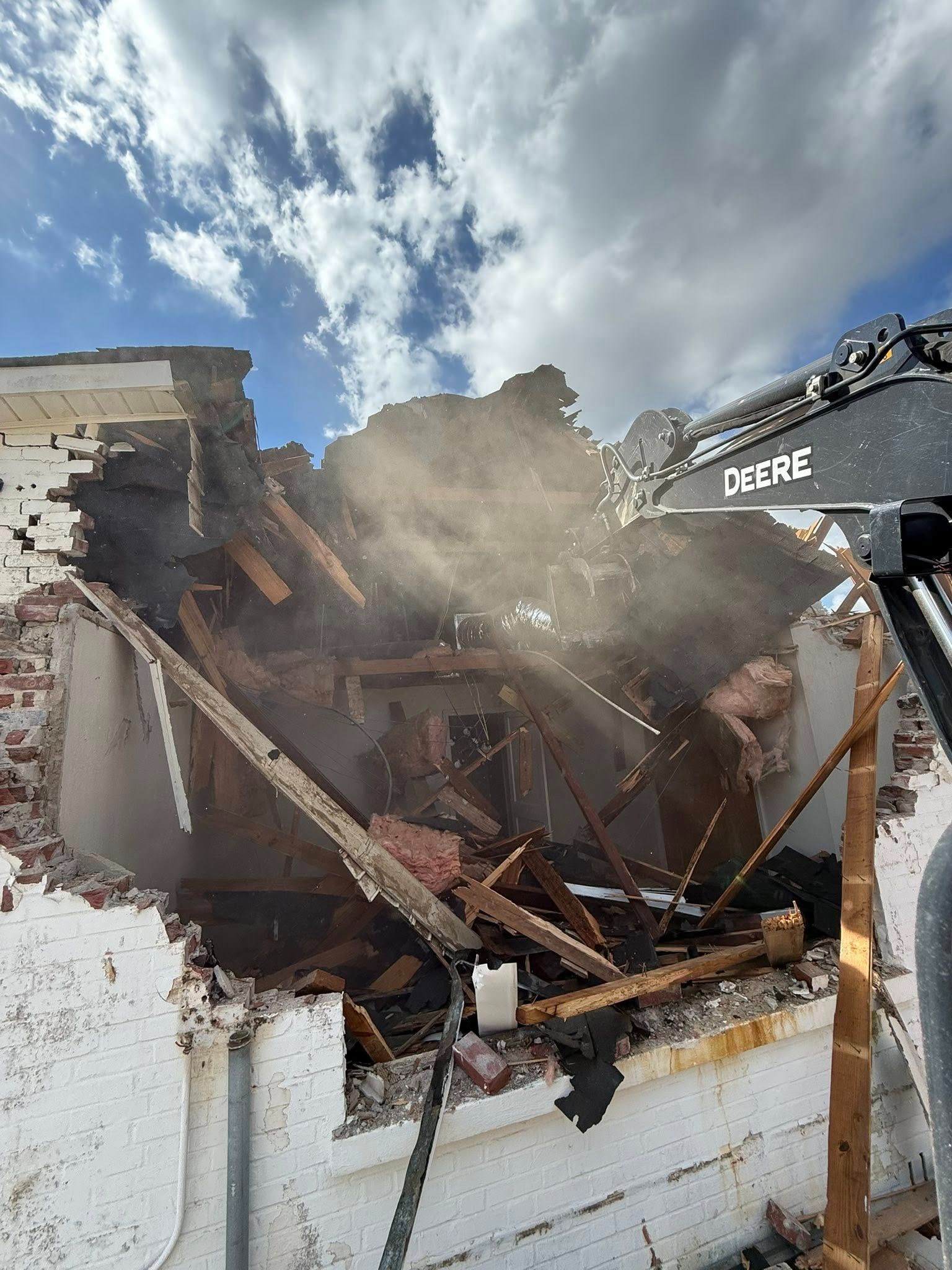 Excavator demolishing a building with a hydraulic hammer, concrete crumbling in the air.