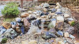 A small outdoor rock water feature with a gentle waterfall cascading down stones into a stream bed.