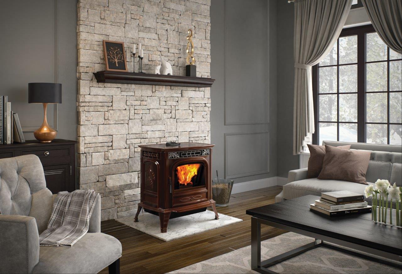 Cozy living room with a burning fireplace and a stone accent wall. A dark brown stove sits on a white rug, with a gray couch and armchairs nearby.