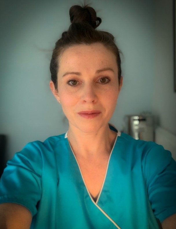 Woman in teal scrubs with hair in a bun looks at the camera.