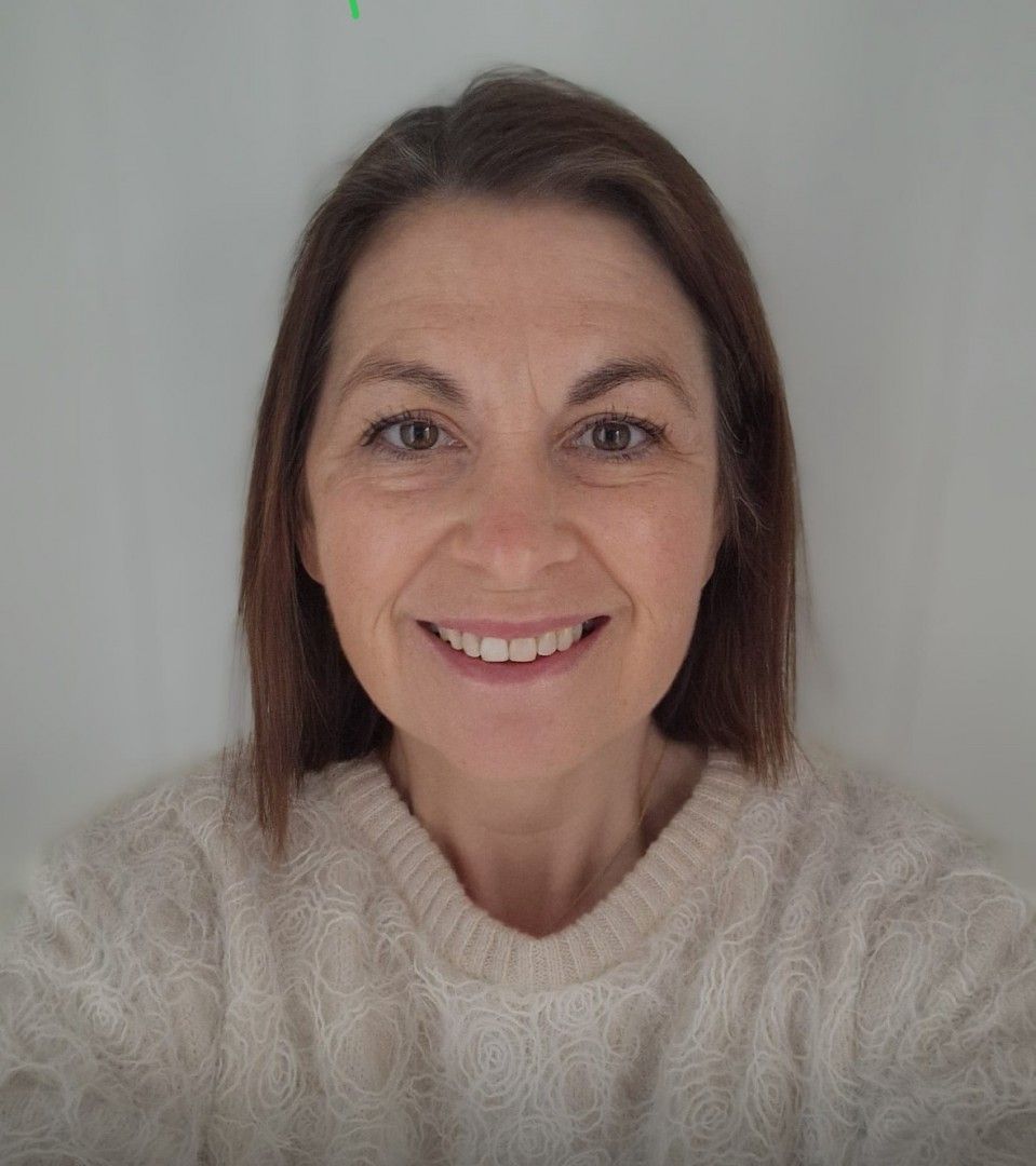 Woman smiling in a cream-colored sweater against a plain white background.
