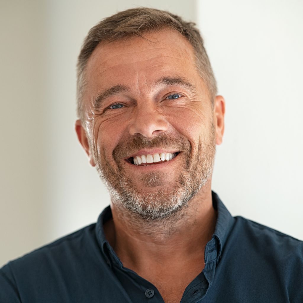 Smiling man with short, graying hair and beard wearing a blue shirt.
