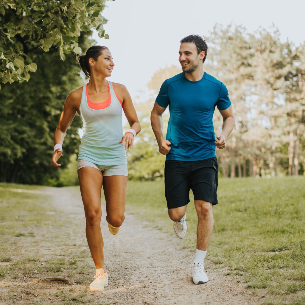 A man and woman running together on a path in a park, smiling.