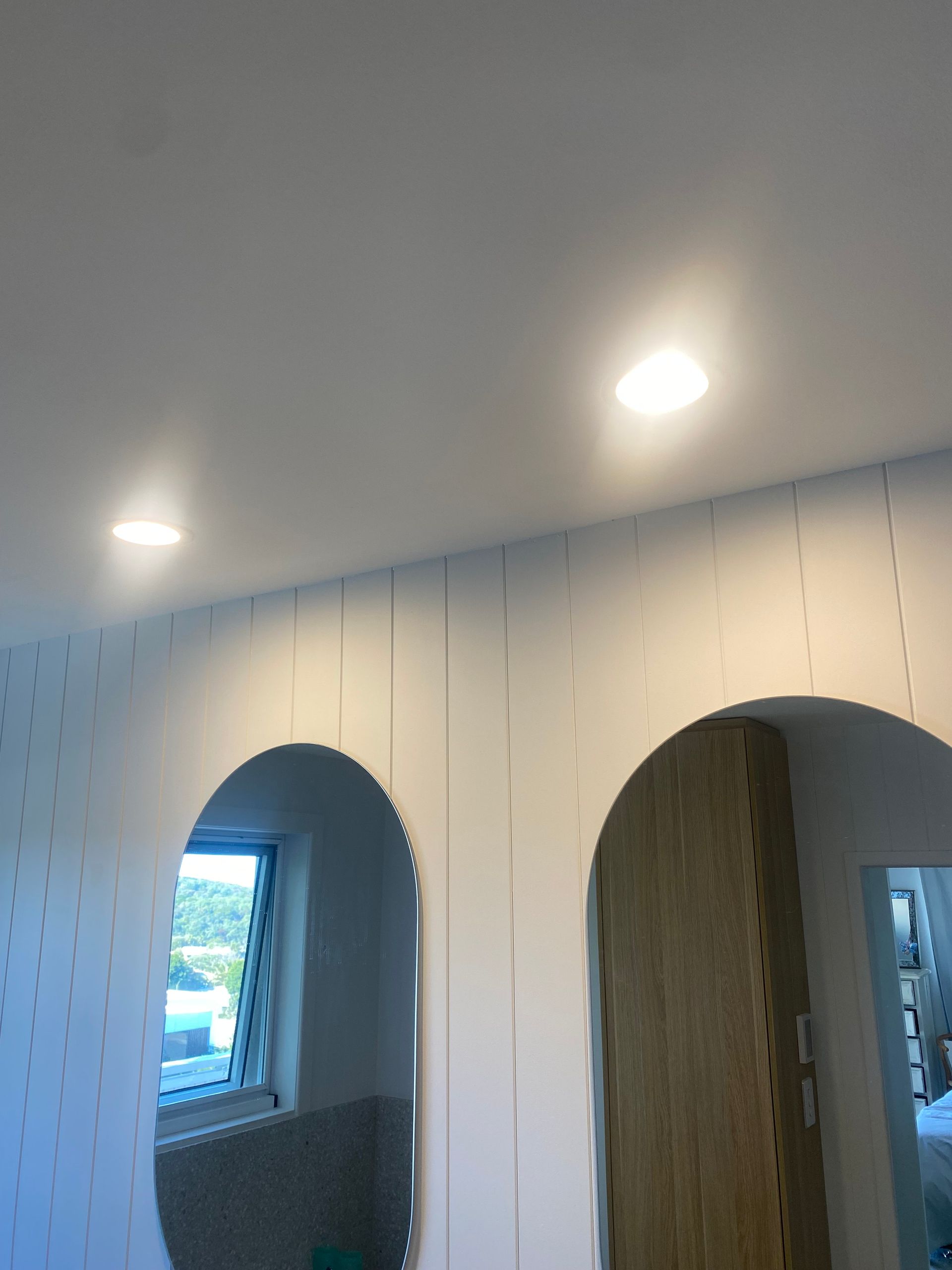 White room with arched doorways, inset ceiling lights, and vertical wall paneling.