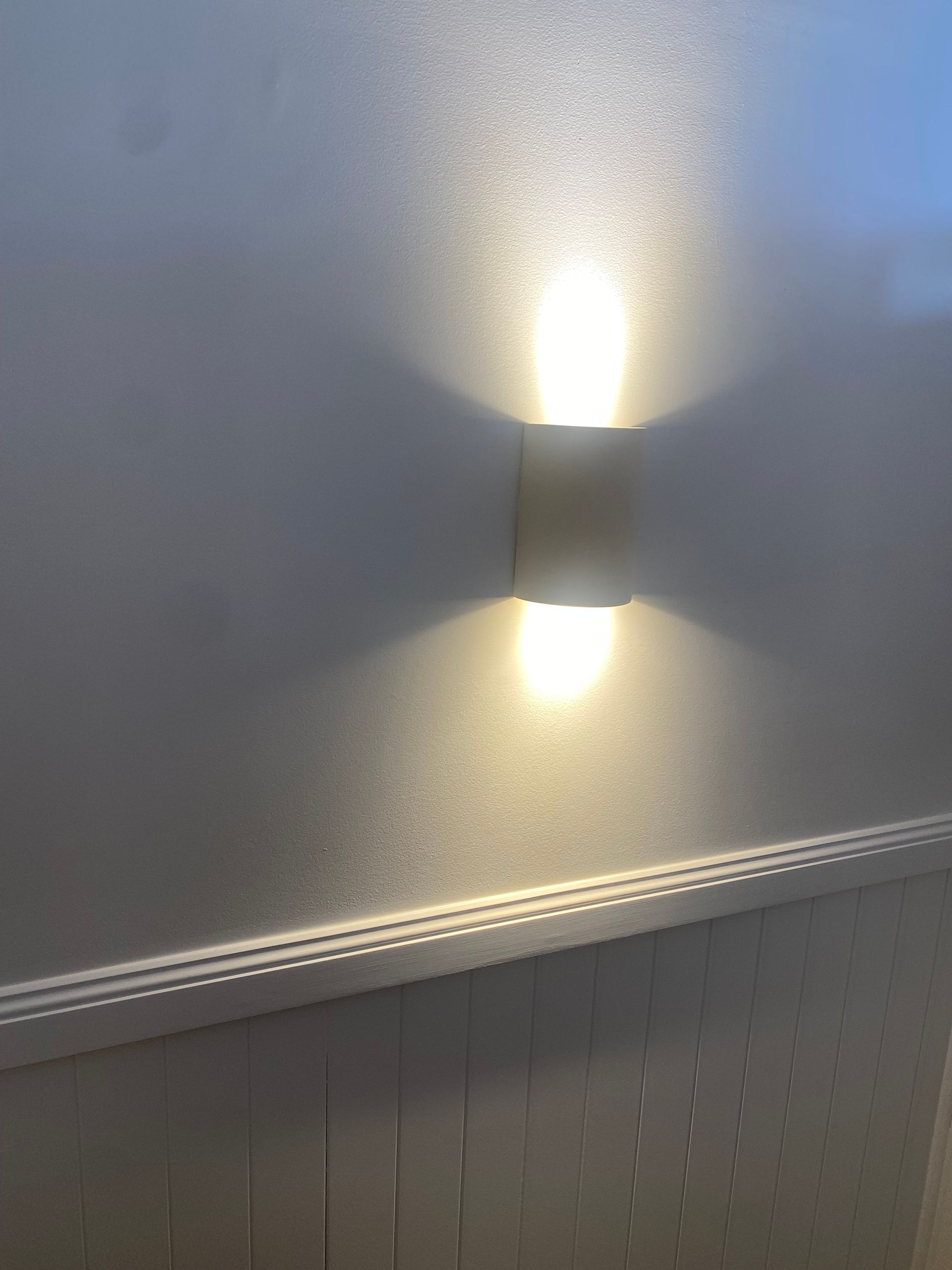 Wall-mounted light fixture casting up and down light on a textured, white surface.